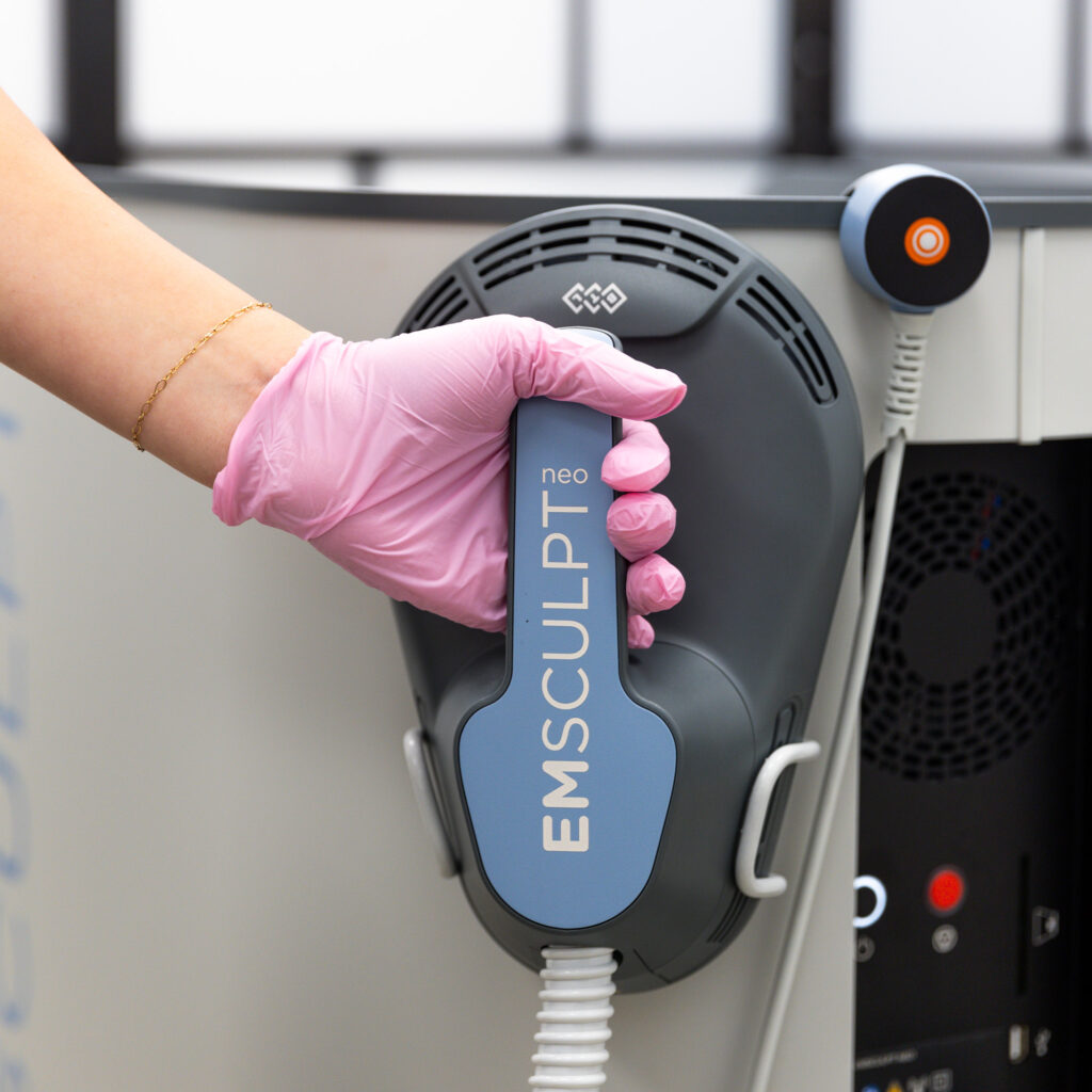 A provider's hand in a pink glove reaches for the Emsculpt NEO device, preparing for our noninvasive mommy makeover in Winter Garden.